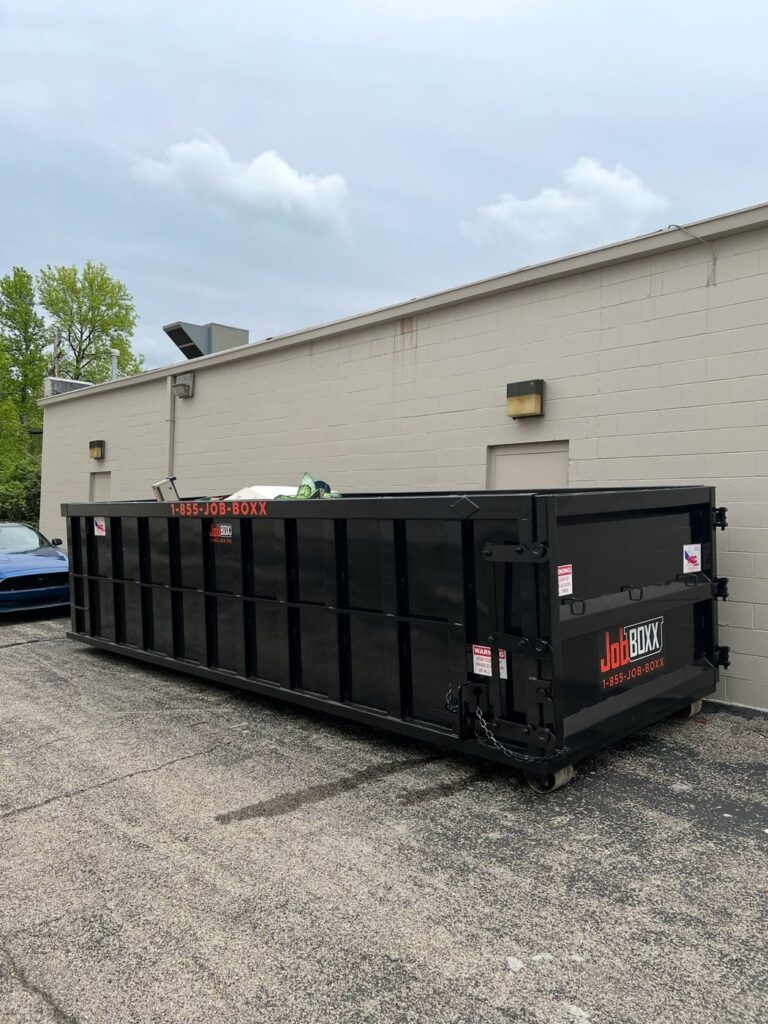 Roll-off container set alongside a commercial building, loaded and ready for pickup